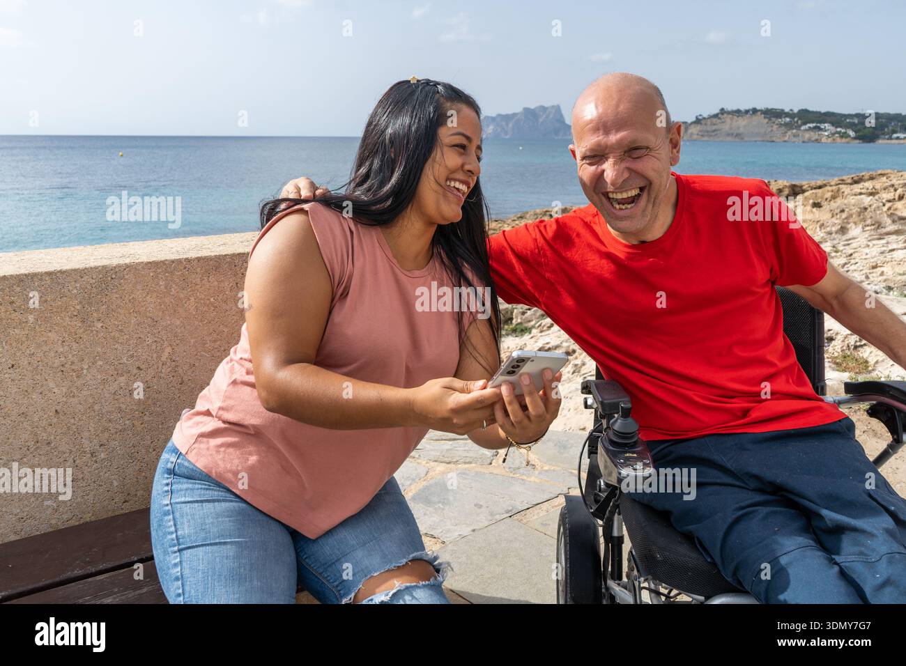 Un momento allegro tra amici all'aperto, con un'attenzione particolare all'inclusività. La scena cattura un uomo su una sedia a rotelle e una donna che condivide una risata con la S. Foto Stock