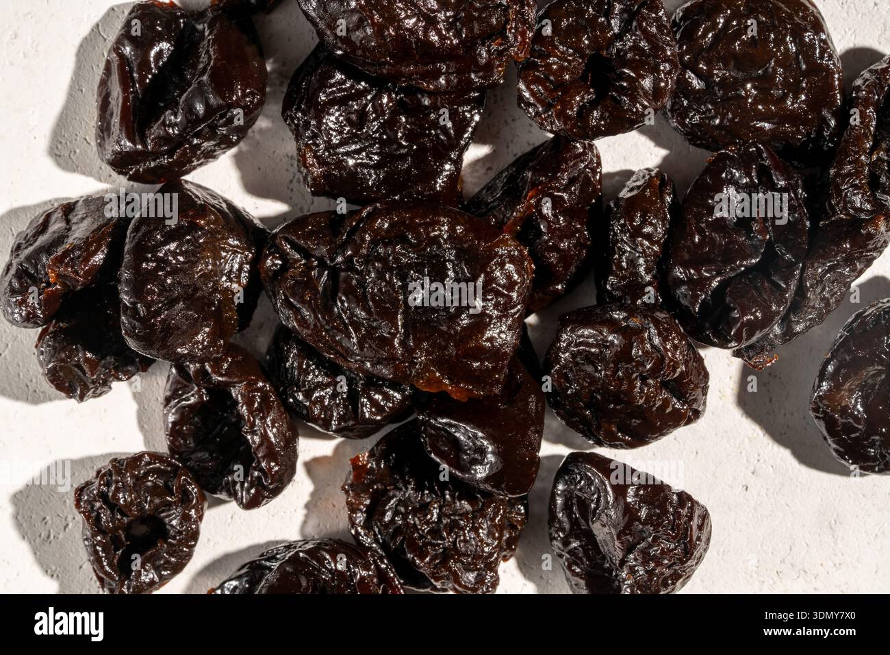 Immagine ravvicinata di prugne secche su una superficie liscia e ruvida. La texture scura e rugosa delle prugne è evidenziata, mostrando i loro colori intensi e. Foto Stock