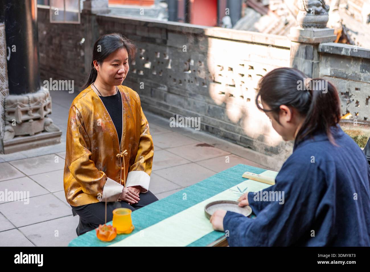 Una serena cerimonia del tè che si svolge all'aperto, dove due donne in abbigliamento tradizionale sono impegnate in un rituale culturale con particolare attenzione alla consapevolezza e al tr Foto Stock