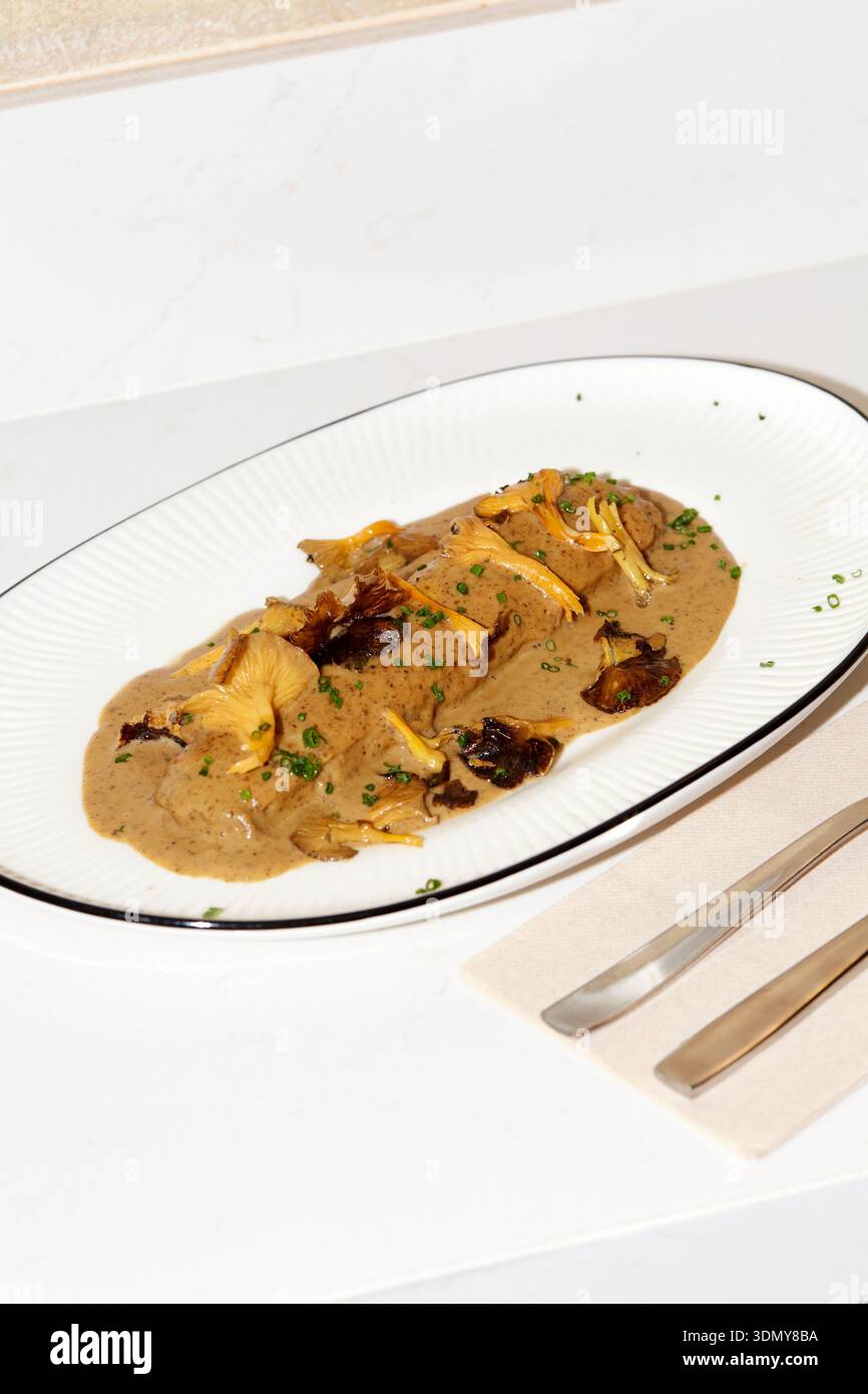 Assapora un piatto di squisiti cannelloni di funghi conditi con ricca salsa cremosa, splendidamente presentati in un moderno ambiente ristorante. Perfetto per i buongustai Foto Stock