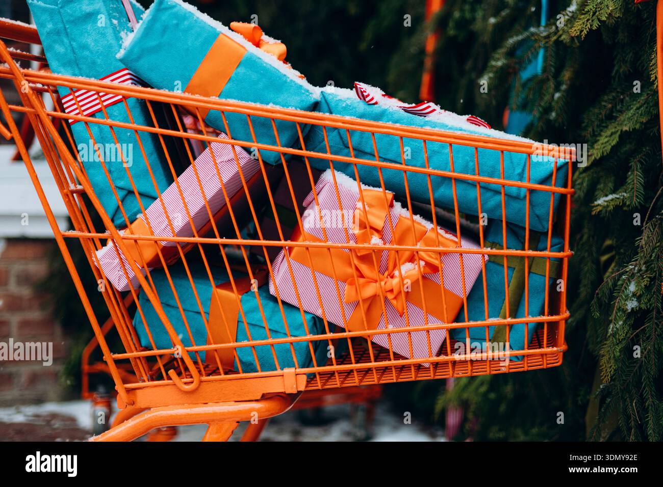 Un luminoso carrello della spesa pieno di regali splendidamente avvolti in colori vivaci, annidato tra il verde del fogliame, per creare un ambiente natalizio per le feste Foto Stock