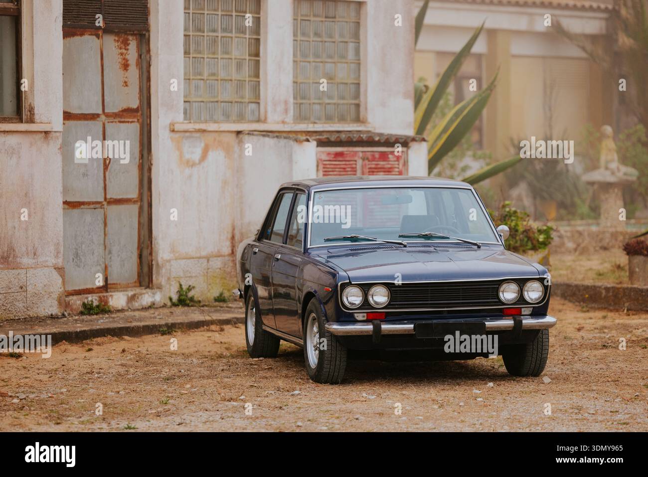 Un'auto d'epoca dal design classico è parcheggiata accanto a un vecchio edificio intempestivo. La scena cattura una visione nostalgica, combinando l'eleganza dell'auto Foto Stock