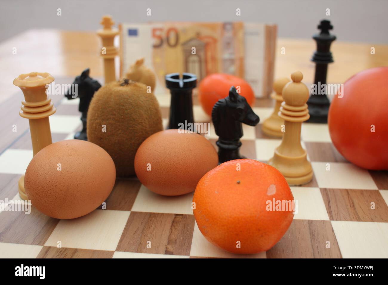 La presenza di prodotti alimentari di uso quotidiano accanto ai pezzi degli scacchi suggerisce un gioco finale teso in cui i consumatori devono ripensare le priorità e la spesa. Foto Stock