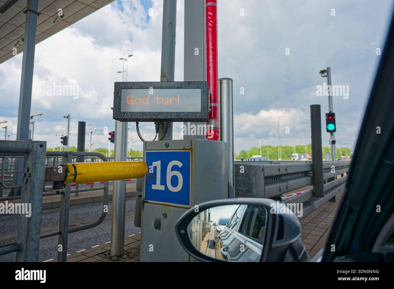 Un indicatore della corsia di pedaggio di OEresund mostra il numero sei e la parola Godtur, visibile accanto al finestrino laterale sinistro e allo specchietto. Un'auto grigia si riflette nel vetro come dri Foto Stock