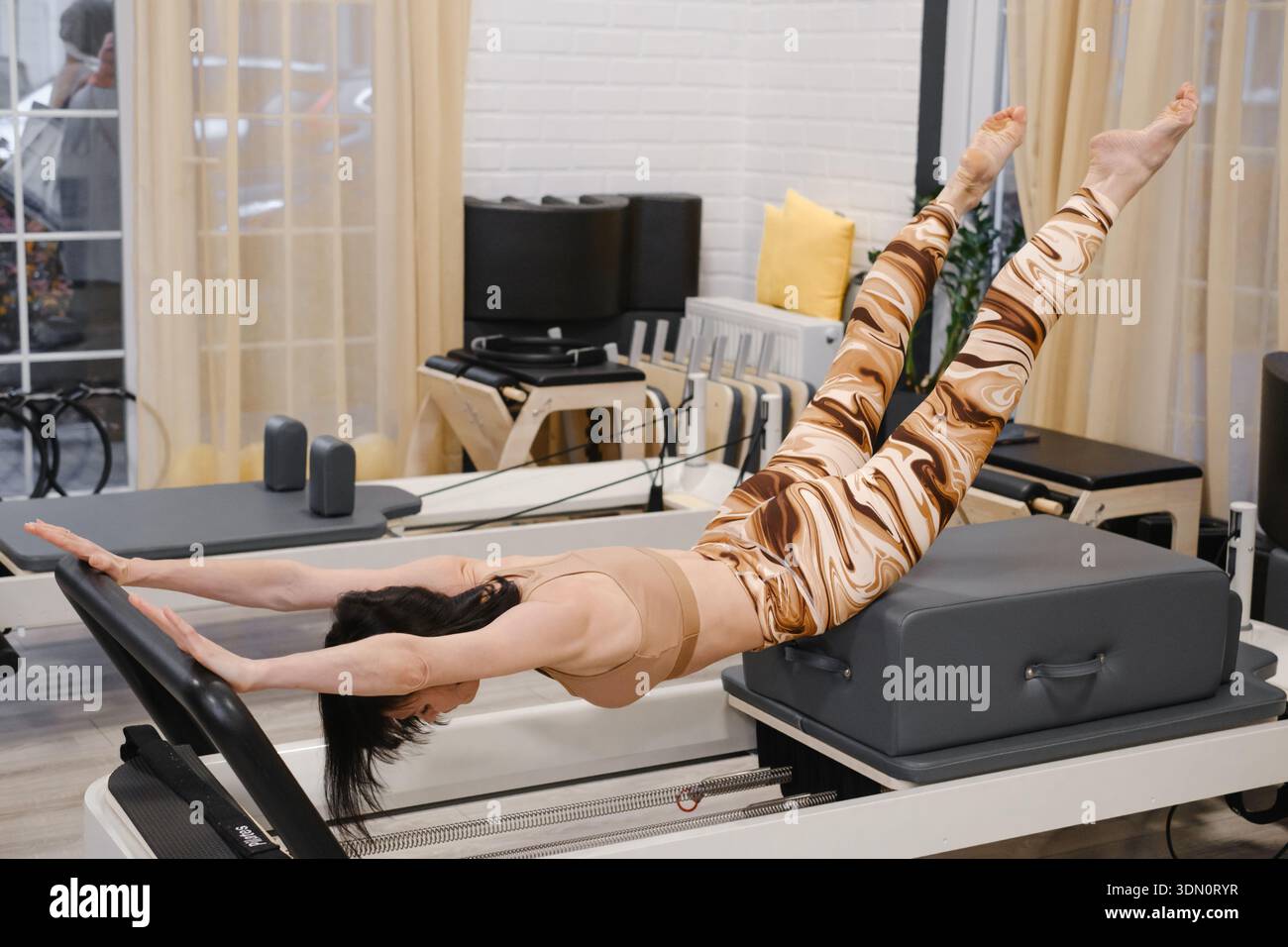Donna matura di 40 anni che esegue pilates riformatori avanzati in esercizi di equilibrio in piedi per la forza e la flessibilità del nucleo. Donna che migliora l'equilibrio Foto Stock