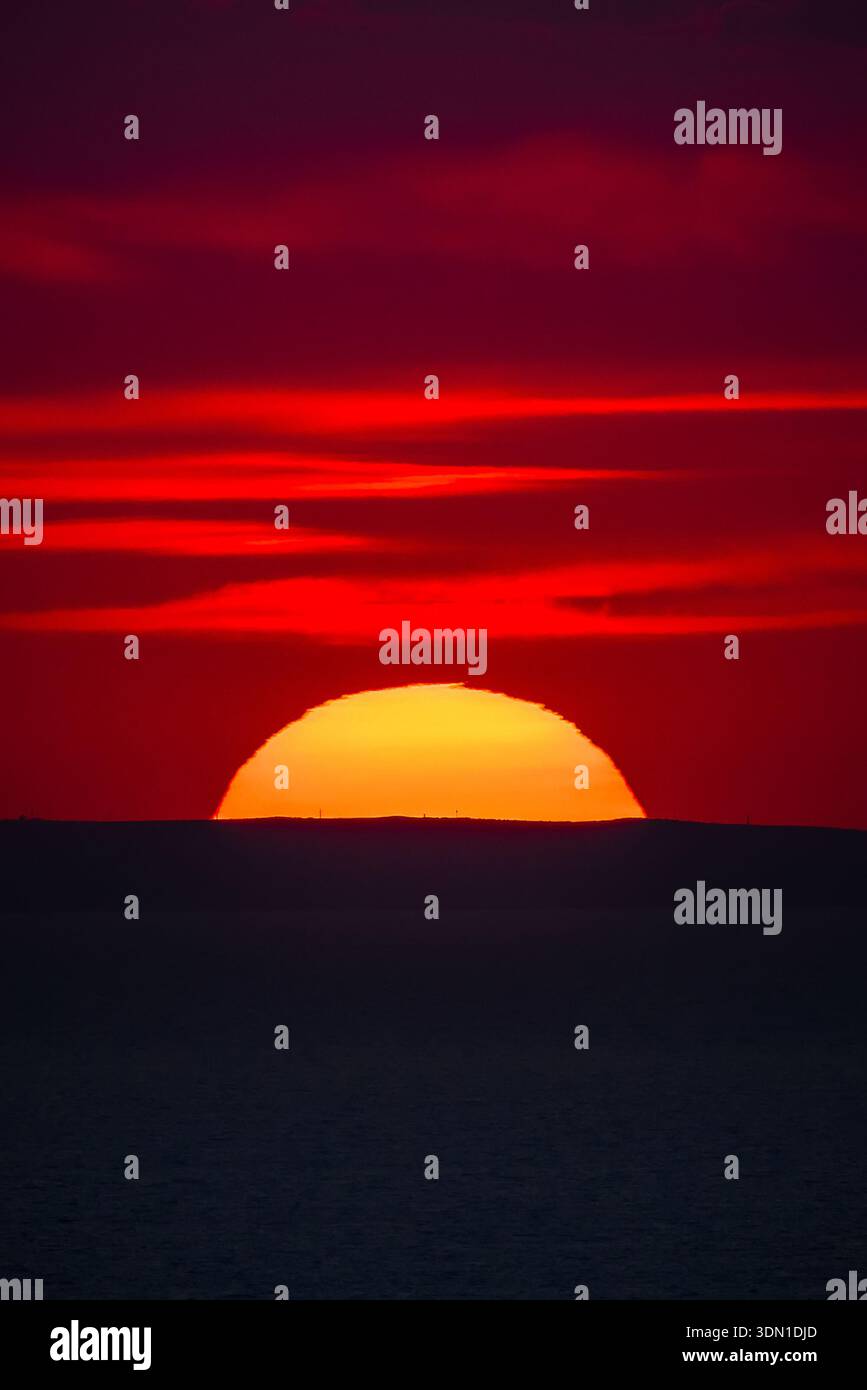 Tramonto rosso sull'orizzonte del mare con una silhouette scura di colline lontane. Foto Stock