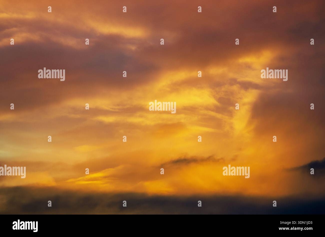 Spettacolare cielo al tramonto con vivaci nuvole arancioni e gialle che creano un'atmosfera infuocata Foto Stock