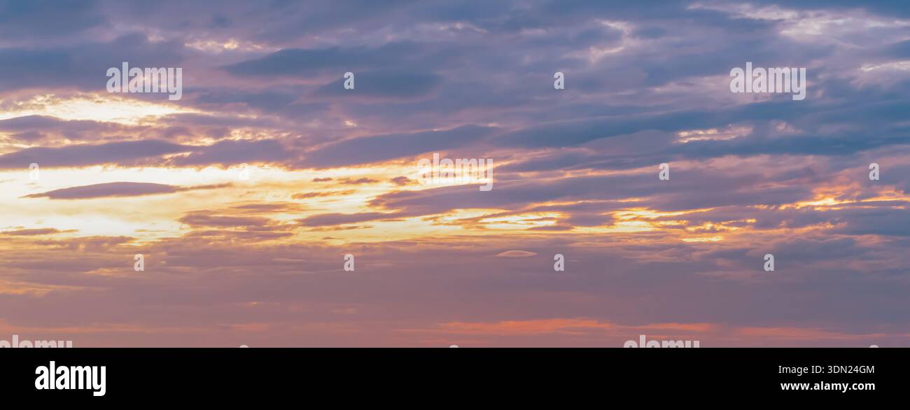 Le nuvole si estendono attraverso il cielo al tramonto, mostrando varie sfumature di arancione e viola mentre la luce si affievolisce. La scena cattura i cambiamenti nel cielo serale Foto Stock