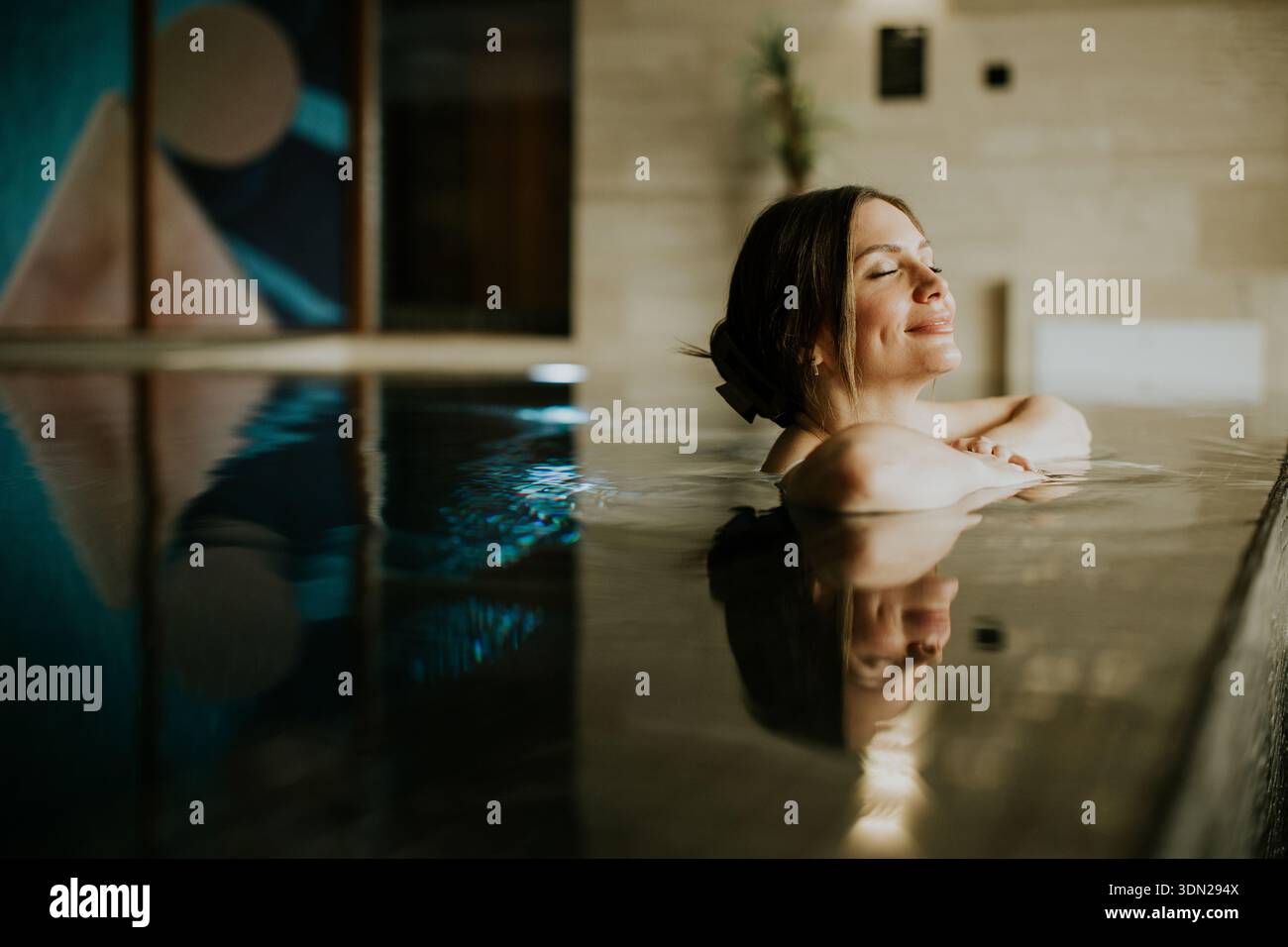 La donna ama trascorrere il tempo libero in una piscina coperta. Si piega indietro con gli occhi chiusi e l'acqua riflette l'opera d'arte nelle vicinanze. L'impostazione ha Foto Stock