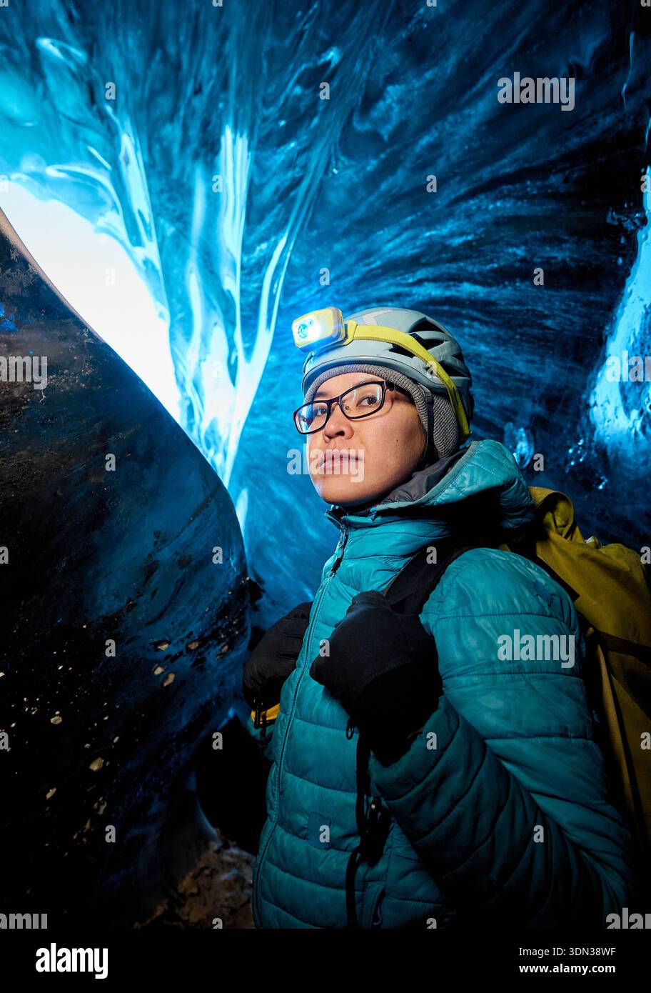 Alpinista scalatore con faro luminescente in una grotta di ghiaccio glaciale buia e profonda con luci blu esplora il ghiacciaio invernale di montagna in Kazakistan Foto Stock
