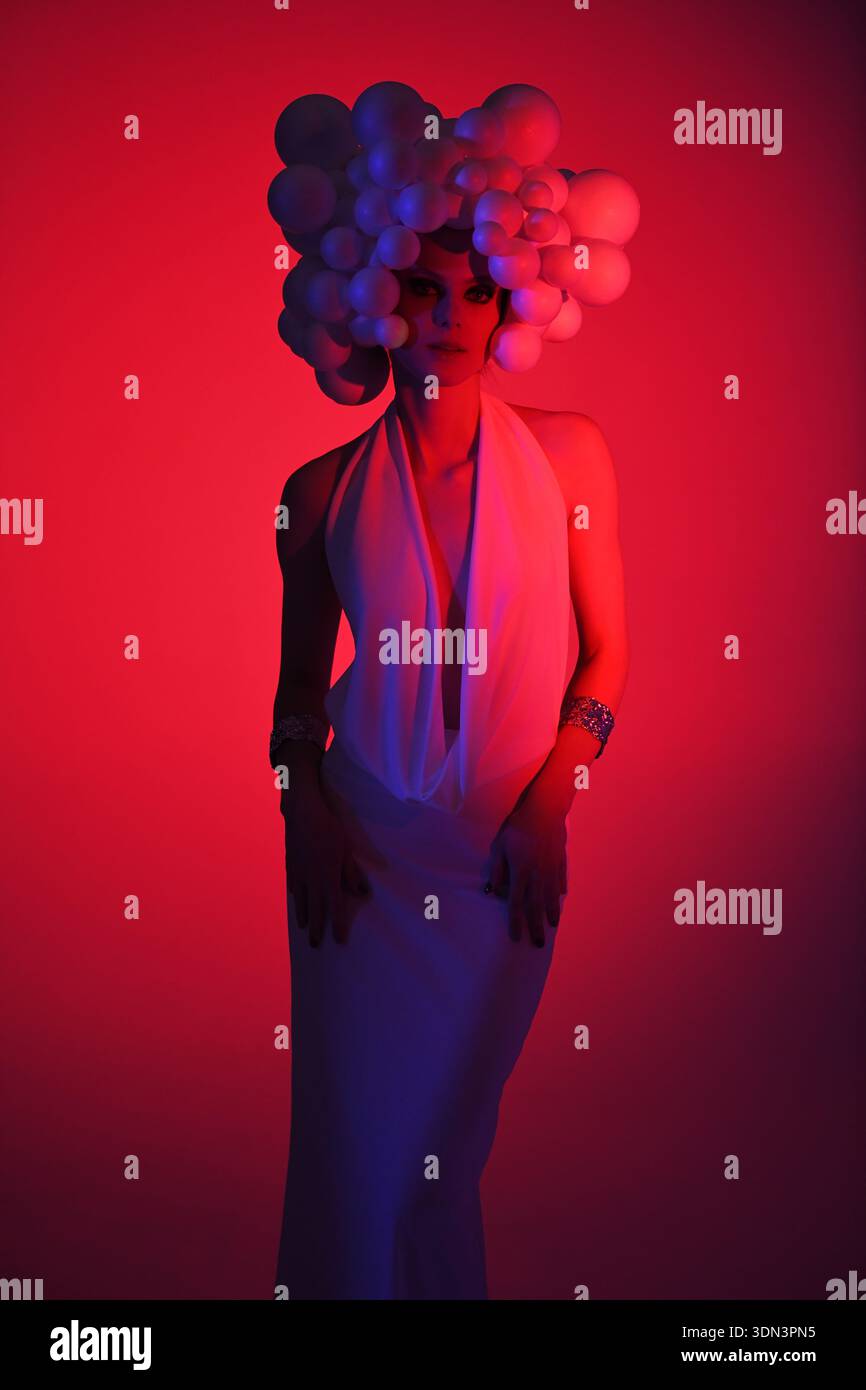 Donna in posa in stile futuristico con un capo scultoreo sotto una vivace luce rossa e blu Foto Stock