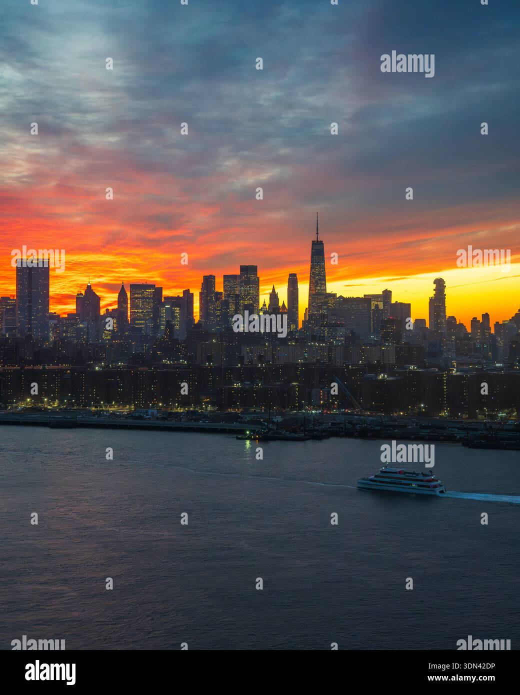 Veduta dello skyline della citta' che si staglia contro un tramonto ardente, con una barca che scivola sull'acqua scura, creando un contrasto vibrante, New York, New Yor Foto Stock