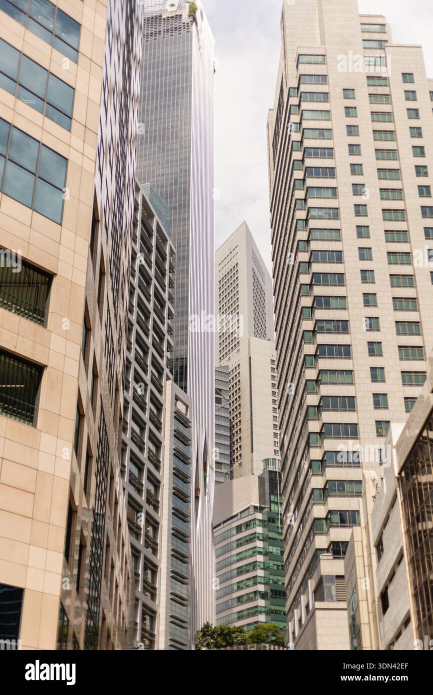 Edifici di varie altezze fiancheggiano una strada in una città trafficata. Le strutture in vetro e calcestruzzo sono vicine tra loro, creando un passaggio stretto. Il cielo è o Foto Stock