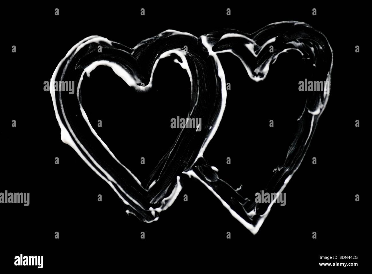 Due forme di cuore lucide disegnate a mano con effetto vernice in vetro su sfondo nero per temi d'amore dal design romantico e progetti creativi Foto Stock