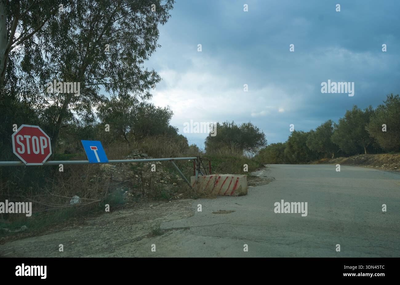 Una strada rurale bloccata nella campagna cretese con un segnale di stop e barriere in cemento. Simboleggia l'accesso limitato e l'infrastruttura locale. Foto Stock