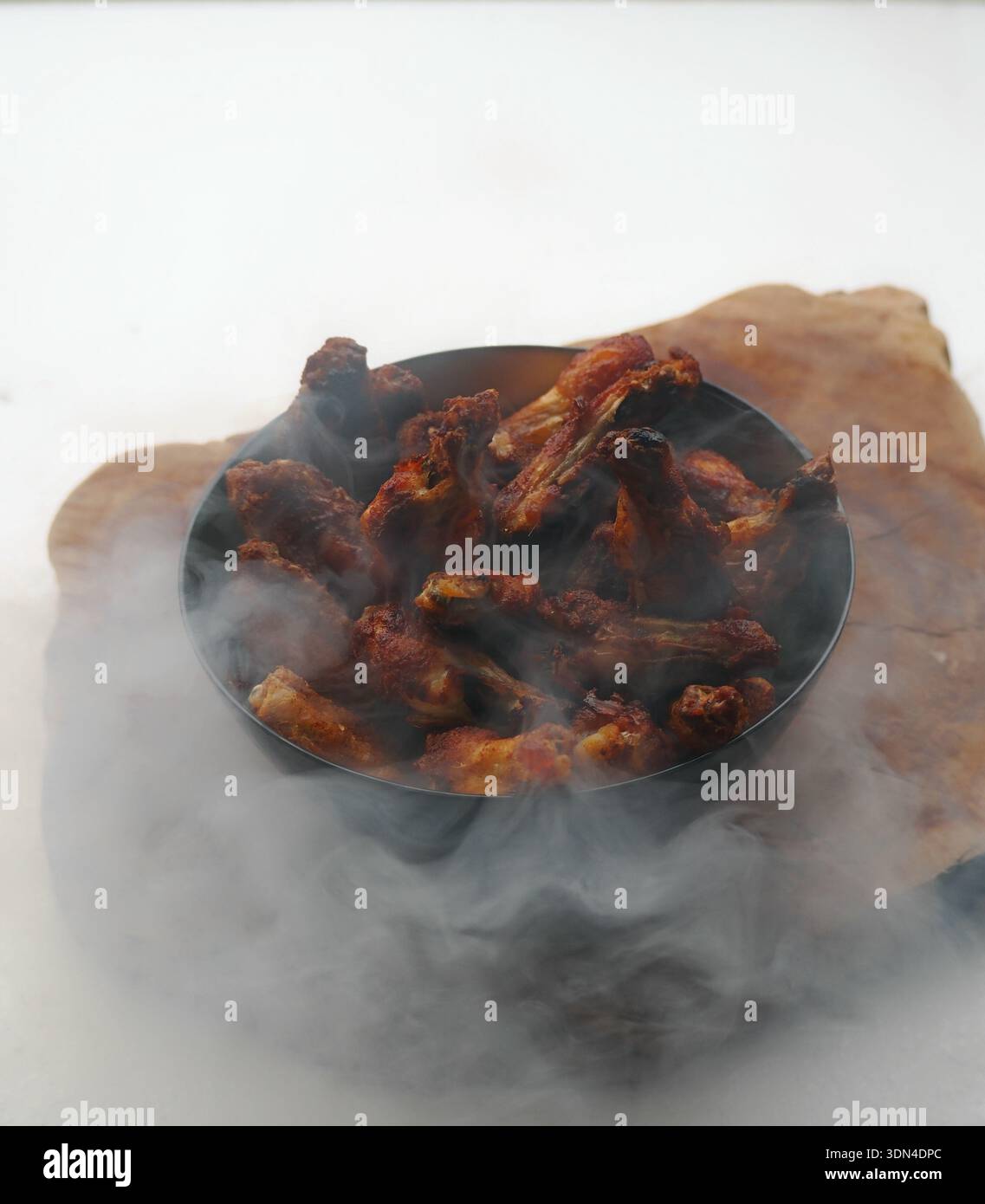 Ciotola di ali di pollo affumicate circondata da fumo drammatico per lo styling del cibo, creando una presentazione barbecue rustica con un'atmosfera oscura e suggestiva. Foto Stock