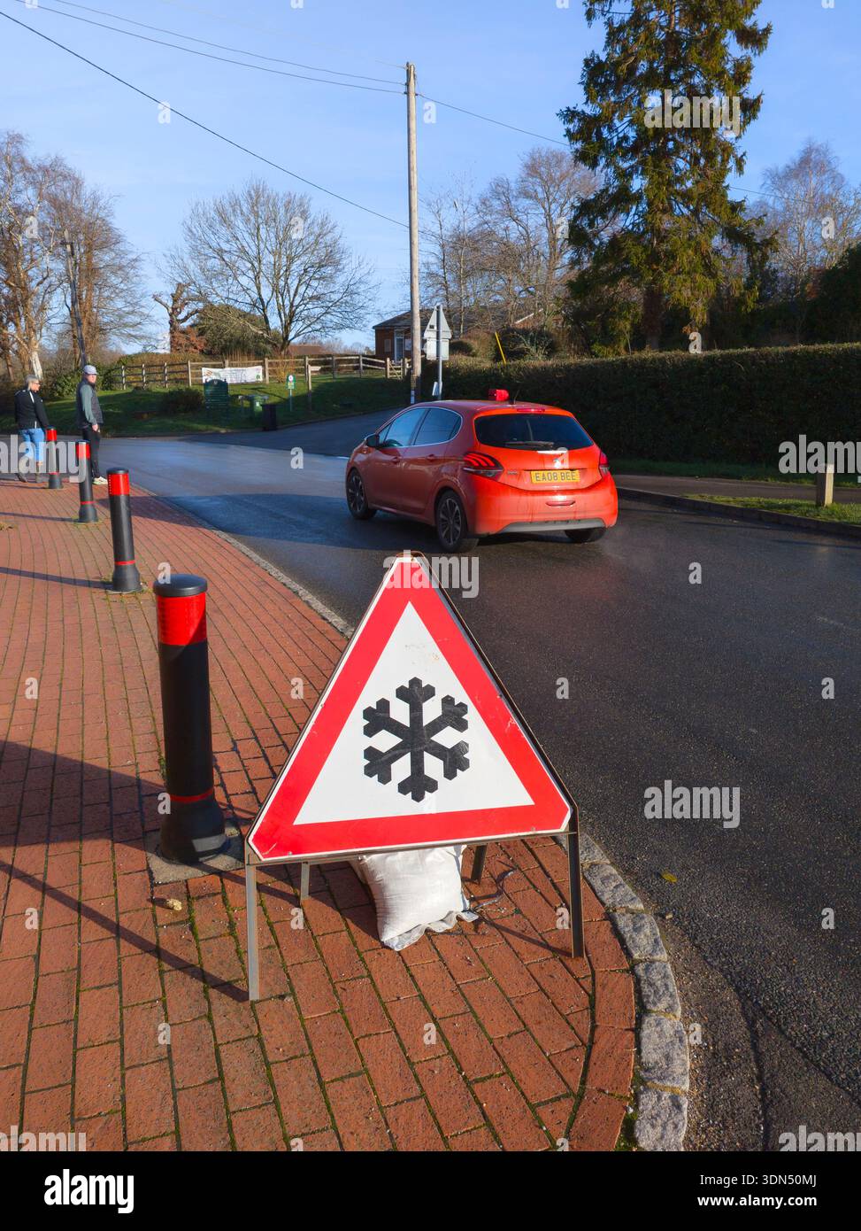 Segnale di avvertimento triangolo rosso per rischio di ghiaccio (diagramma DOT 554 del Dipartimento dei trasporti) in una giornata invernale con un'auto che passa accanto, a Basingstoke, Regno Unito - Immagine stock catturata con smartphone