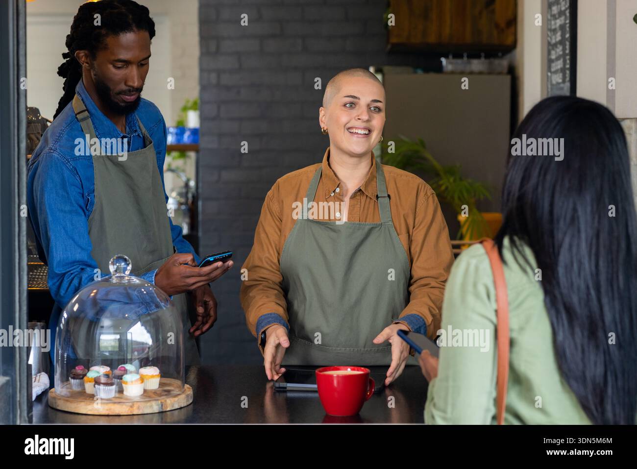 Diversi baristi che servono il caffè alla donna indiana al bancone del caffè e gestiscono verso la tazza rossa Foto Stock