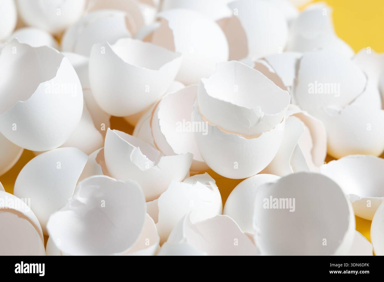 Piccoli pezzi di gusci d'uovo vuoti coprono una superficie gialla in cucina. Le conchiglie mostrano segni di crepe e sbucciature delle uova appena cotte. Foto Stock