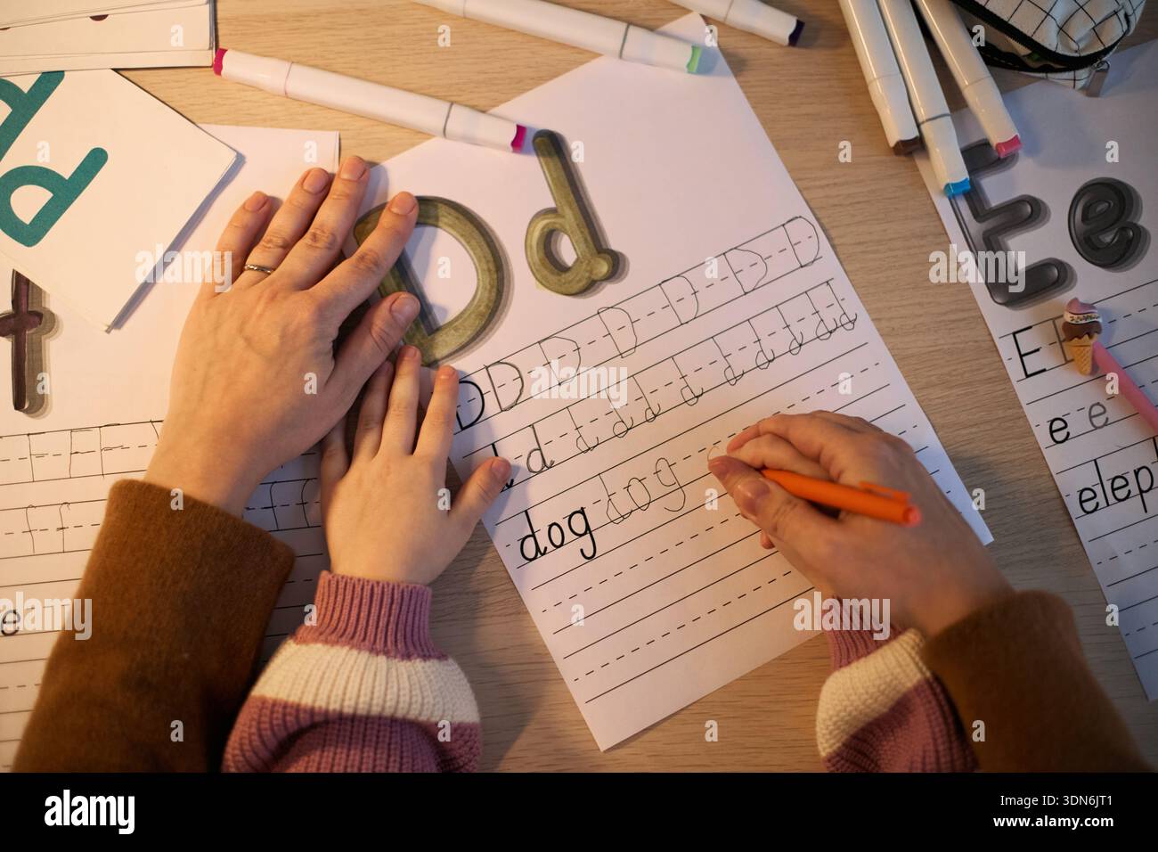 Donna caucasica che guida il bambino caucasico scrivendo lettere su foglio di lavoro, mano adulta che aiuta il bambino a forma di mano, attività educativa che coinvolge la pratica della scrittura a mano alla scrivania Foto Stock