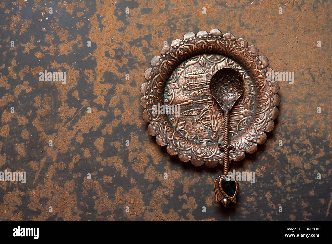 Un piatto decorativo in rame splendidamente realizzato accompagnato da un elegante cucchiaio, ideale per mostrare squisite stoviglie e evocare eleganza e tra Foto Stock