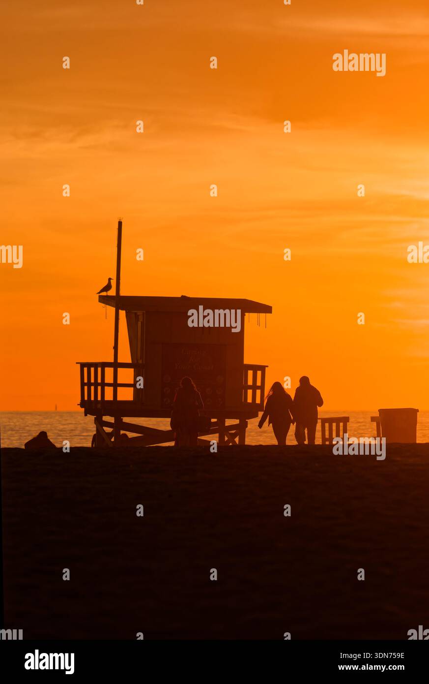 Stazione bagnino al tramonto. Serata tranquilla con coppia che passa davanti alla torre della guardia sotto il cielo incandescente Foto Stock