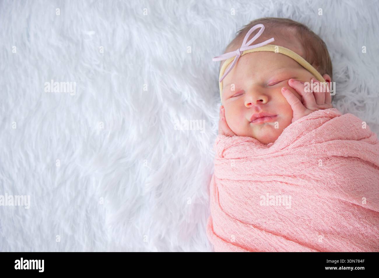 Una bambina appena nata dorme con un pannolino rosa su pelliccia sintetica bianca Foto Stock