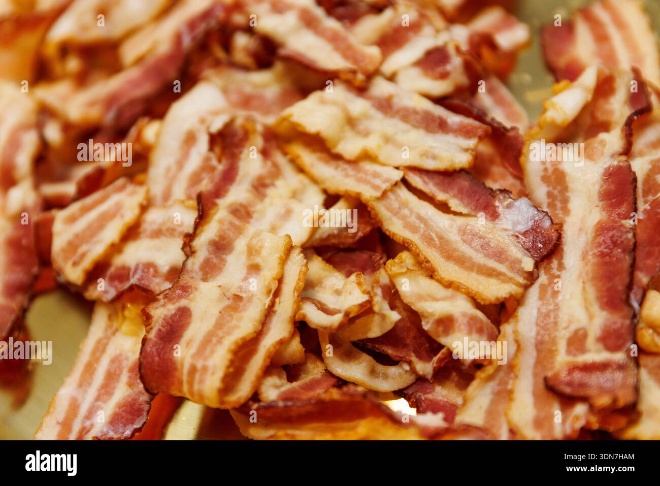 Un mucchio di croccanti strisce di bacon cotte che mostrano consistenza, strati di grasso e colori ricchi. Foto Stock