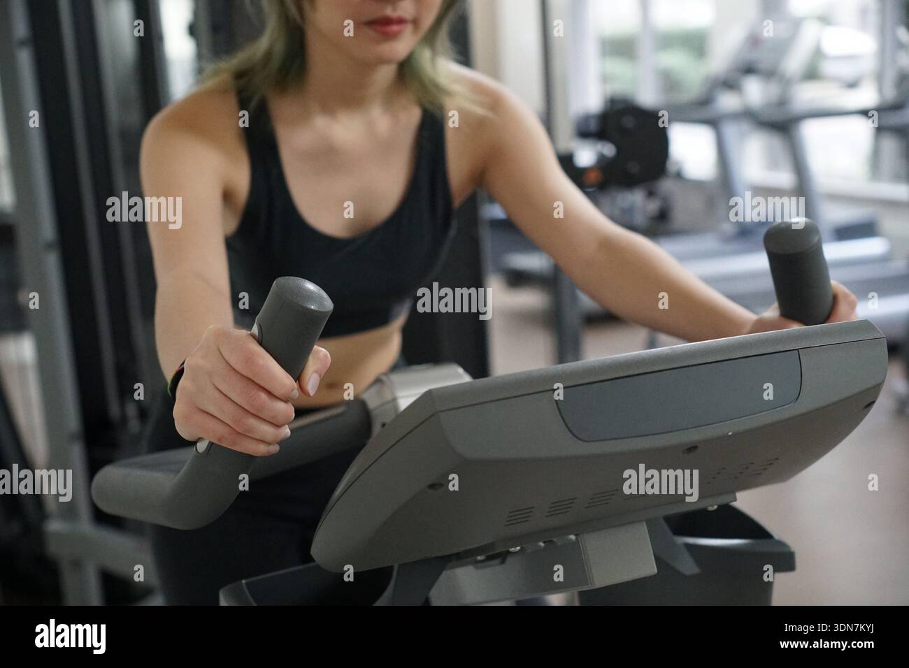 Donna che usa la macchina cardio nella palestra coperta Foto Stock