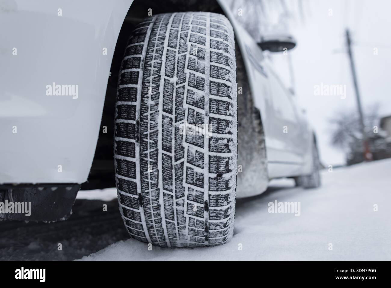 Vista laterale della ruota di un'auto sulla neve, che mostra la protezione e la parete laterale dello pneumatico alla luce del giorno. blocchi del battistrada degli pneumatici invernali riempiti di neve. struttura in gomma. Foto Stock