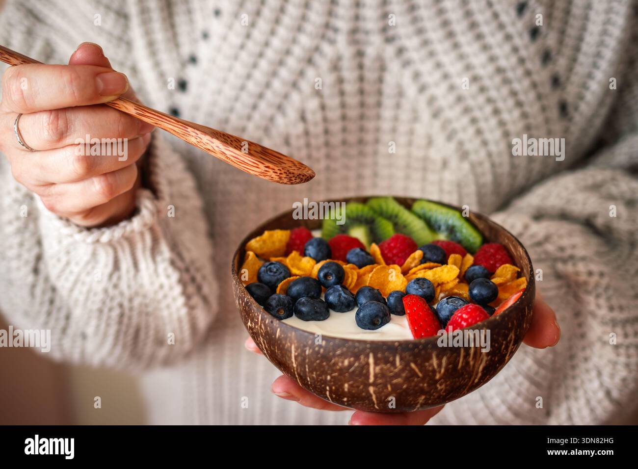 Donna che mangia una sana colazione dalla ciotola di cocco. Yogurt con fiocchi di mais e frutti di bosco Foto Stock