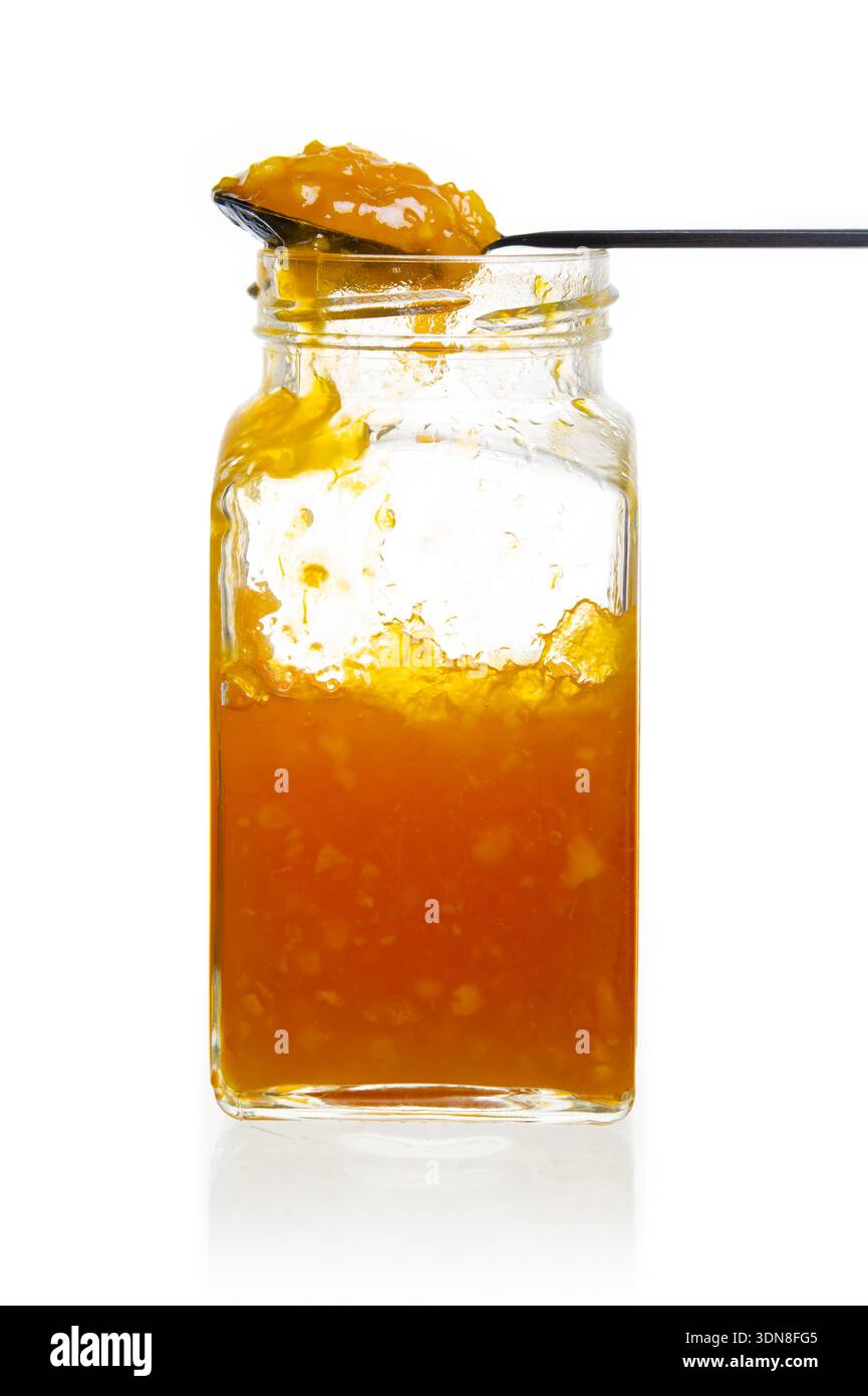 Un primo piano di un vaso pieno di marmellata d'arancia dorata, un cucchiaio pronto da servire, che mostra la sua deliziosa consistenza grossolana e i colori vivaci. Foto Stock