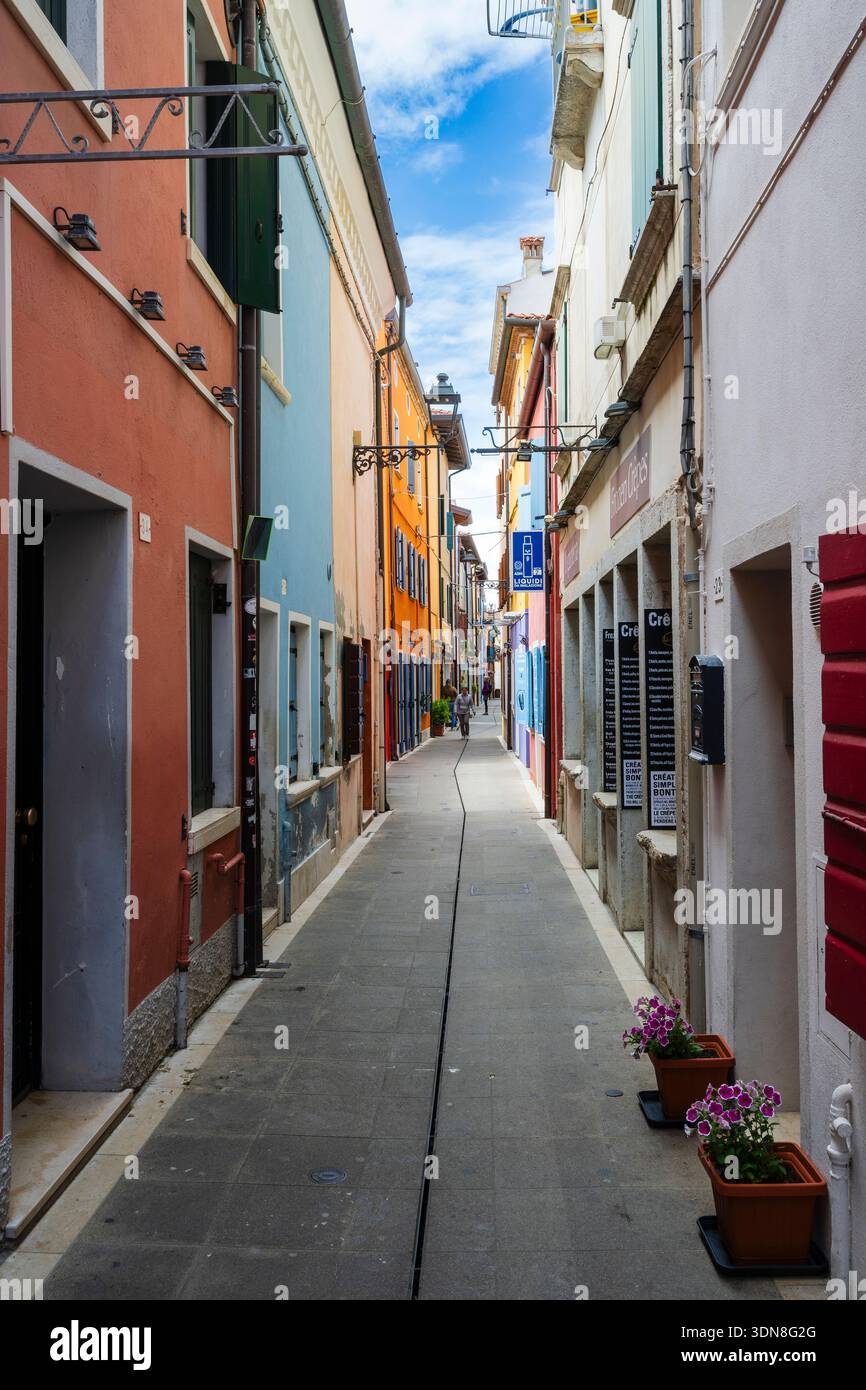 Un vicolo stretto e colorato con edifici vivaci e un cielo azzurro. Caorle, città metropolitana di Venezia, Veneto, Italia Foto Stock