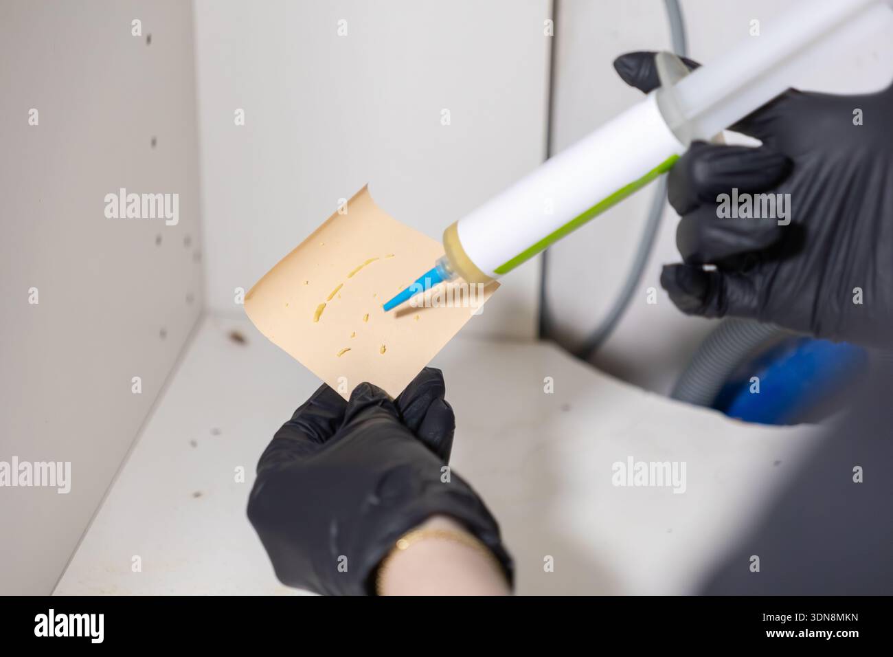 Immagine dettagliata di un operatore del servizio di controllo disinfestante professionista con guanti neri che applica un'esca in gel insetticida a una trappola, mirando efficacemente gli insetti all'interno Foto Stock