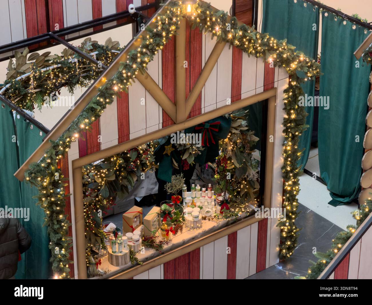 Vista dall'alto di un affascinante bancone del mercatino di Natale, decorato con luci scintillanti festive e ghirlande verdi, che mostrano pezzi unici fatti a mano Foto Stock