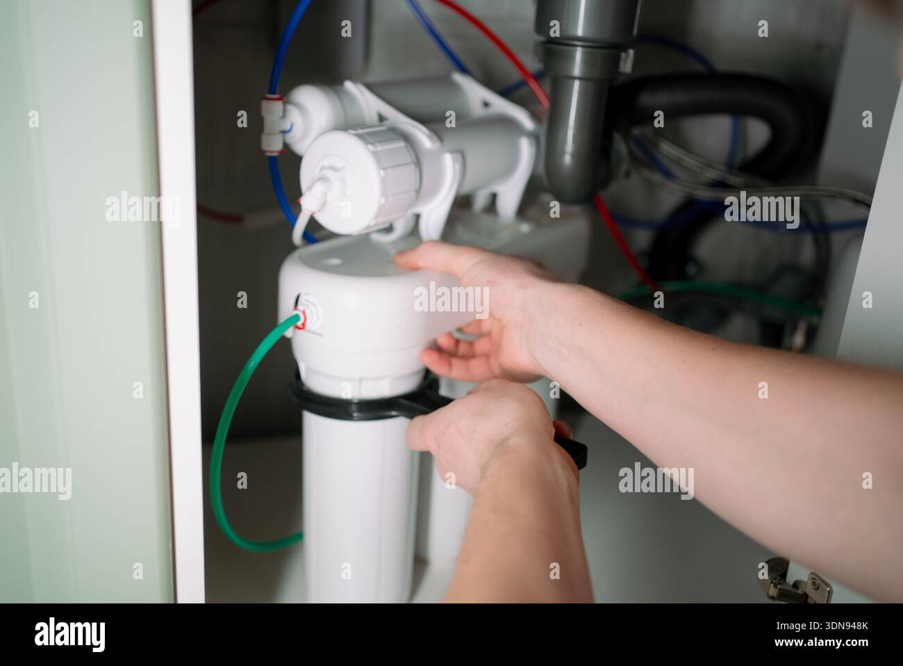 Le mani di una persona che lavora alla sostituzione di una cartuccia del filtro dell'acqua in un sistema di purificazione a osmosi inversa multistadio, garantendo acqua potabile pulita e manutenzione delle tubazioni domestiche Foto Stock