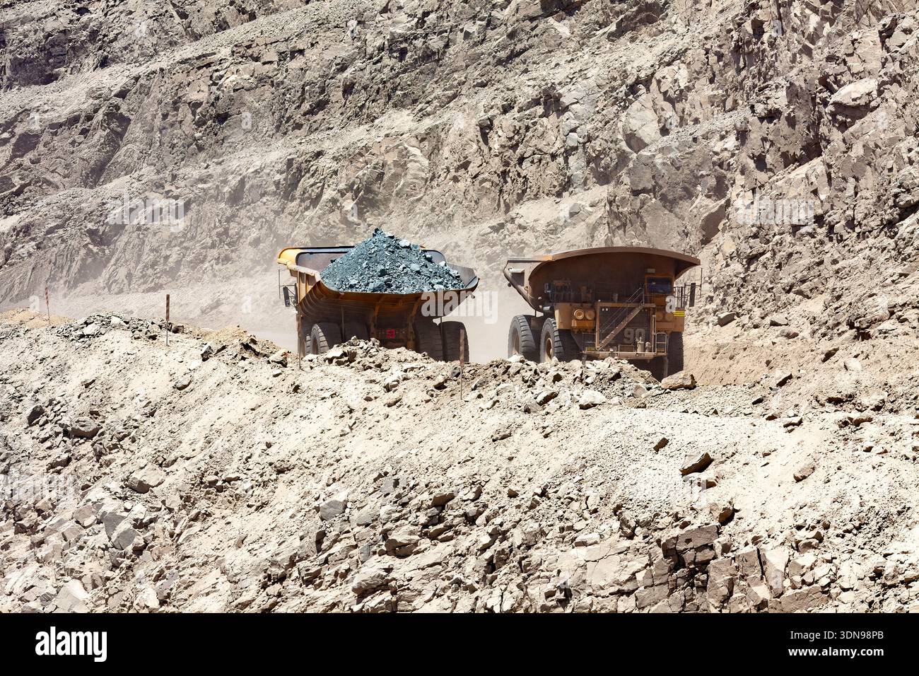 Due enormi camion trasportano minerali di rame grezzi lungo una strada polverosa in una miniera di rame in Cile. Foto Stock