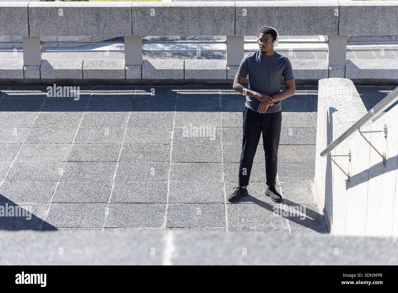 Uomo afroamericano in piedi su una terrazza pavimentata aperta con t-shirt e cuffie atletiche, spazio copia Foto Stock