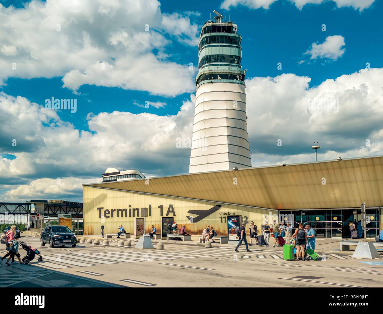 Architettura contemporanea di un edificio terminale e di un'importante torre di controllo adagiata su un cielo blu con nuvole bianche nell'aeroporto di Vienna. Foto Stock