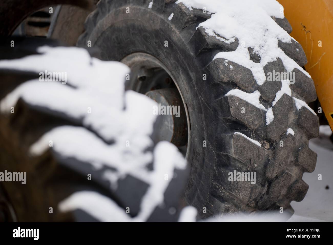 Ruota e battistrada delle attrezzature pesanti innevati con una messa a fuoco nitida, mostrando robusti blocchi in gomma e area del mozzo, con pneumatici fuori fuoco in primo piano Foto Stock