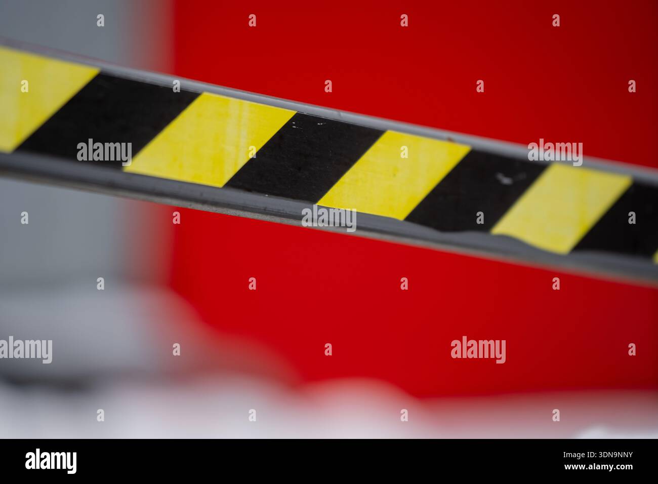Dettaglio selettivo del fascio barriera di sicurezza a strisce in nero e giallo, sottolineando lo schema di segnalazione di pericolo contro la struttura rossa sfocata eq Foto Stock