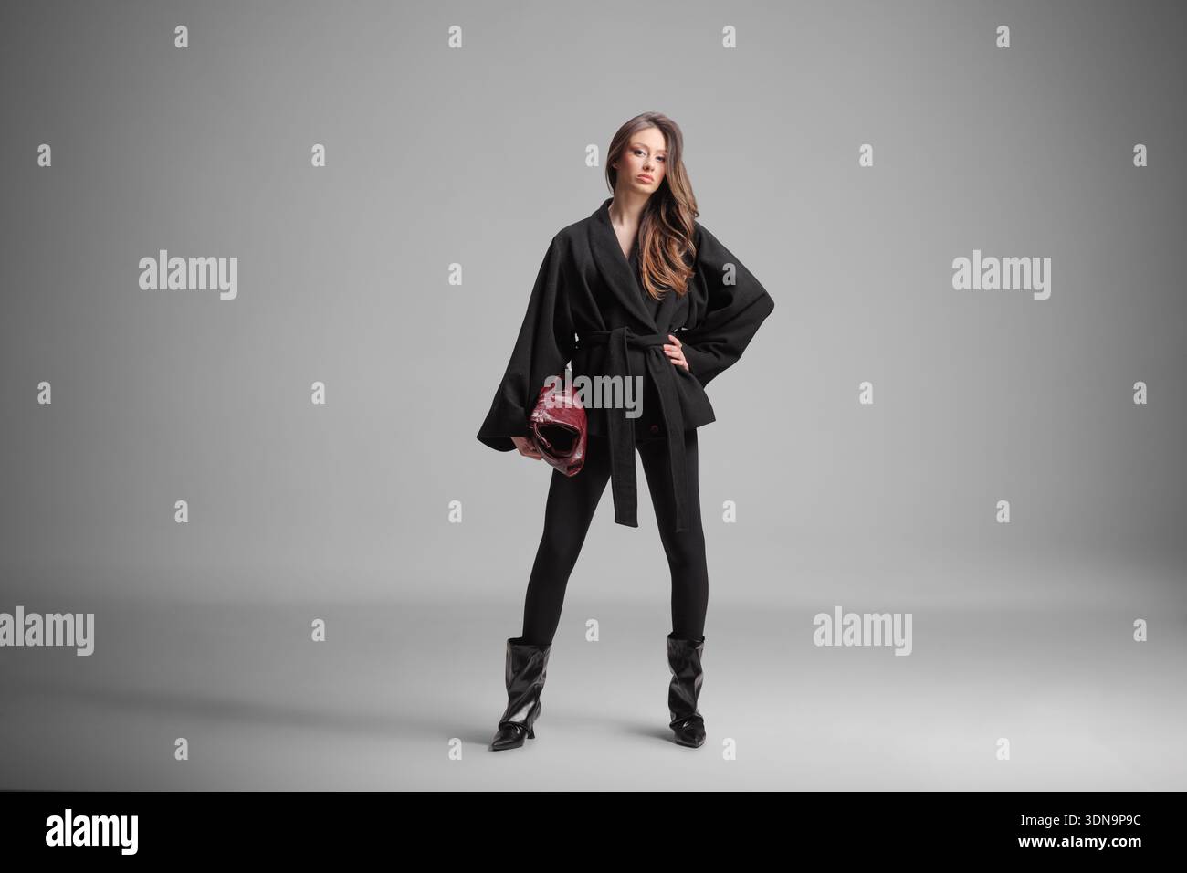 Donna elegante in un cappotto nero con borsa Bordeaux in posa in studio Foto Stock