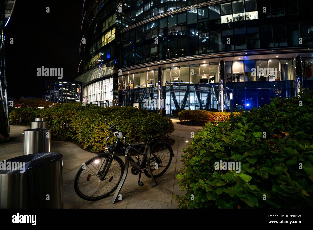 Scena notturna di strada a Varsavia, in Polonia, con una bicicletta parcheggiata sotto le calde luci della città. Atmosfera urbana con toni moody e architettura europea nel Foto Stock