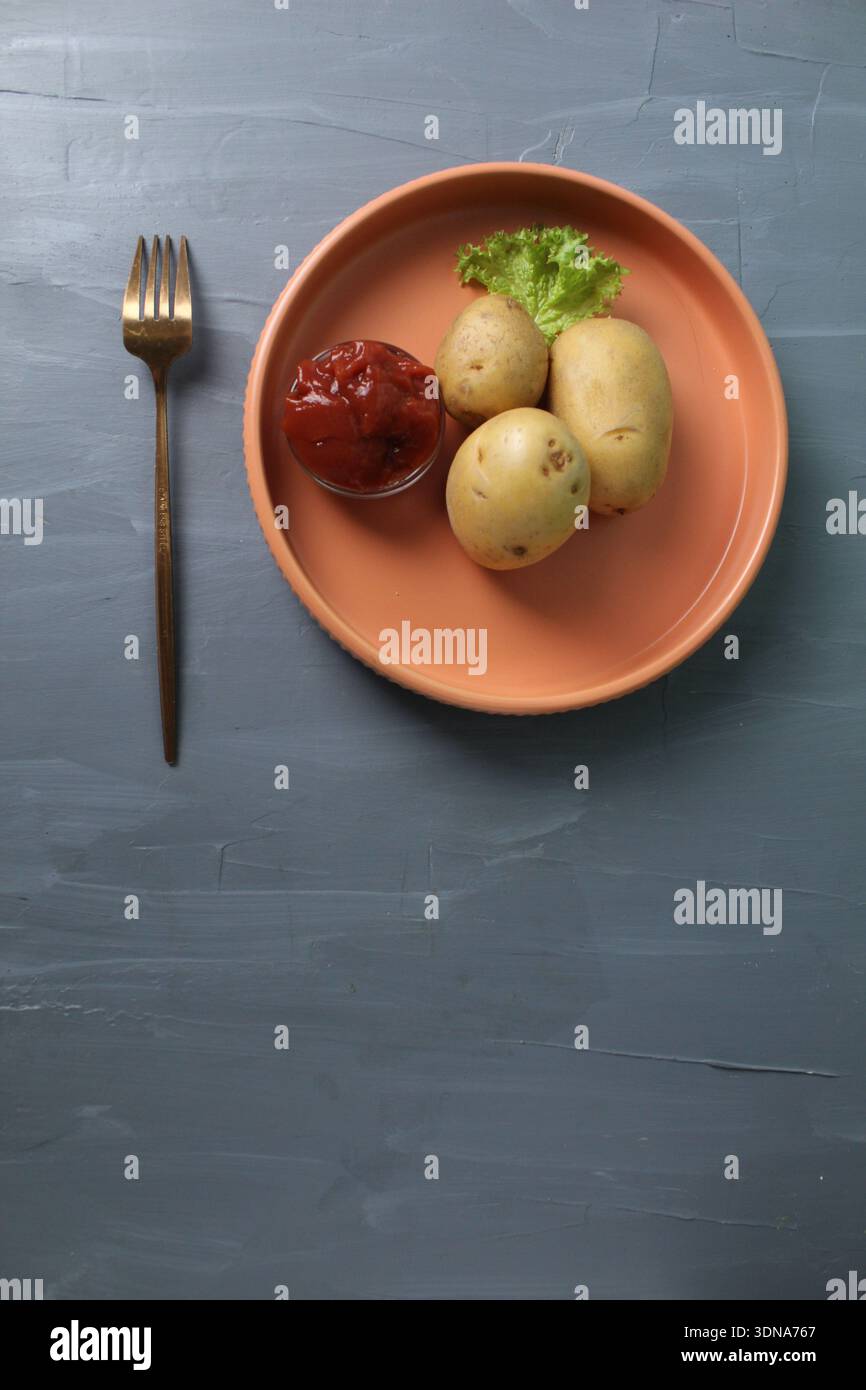 Pranzo servito, patate crude su un piatto, forchetta, tovagliolo su sfondo grigio con spazio per il testo del copyspace. Il concetto di vegetarianismo, rifiuto di carne e pesce. Foto Stock