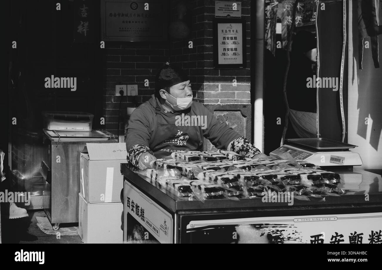 Venditrice mascherata dietro la bancarella di snack al mercato di Yongxingfang in bianco e nero Foto Stock