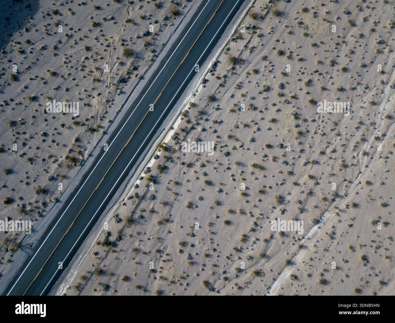 Vista aerea con drone che guarda direttamente in basso su un deserto sparso del Mojave con una strada asfaltata a due corsie che attraversa il telaio diagonalmente Foto Stock