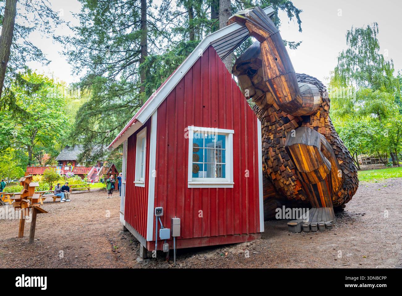 Portland, OREGON, USA - 11 ottobre 2025: Il gigante troll di Ole bolle, realizzato in legno bonificato, sbircia giocosamente in un piccolo cottage rosso sul groun di Fogelbo Foto Stock