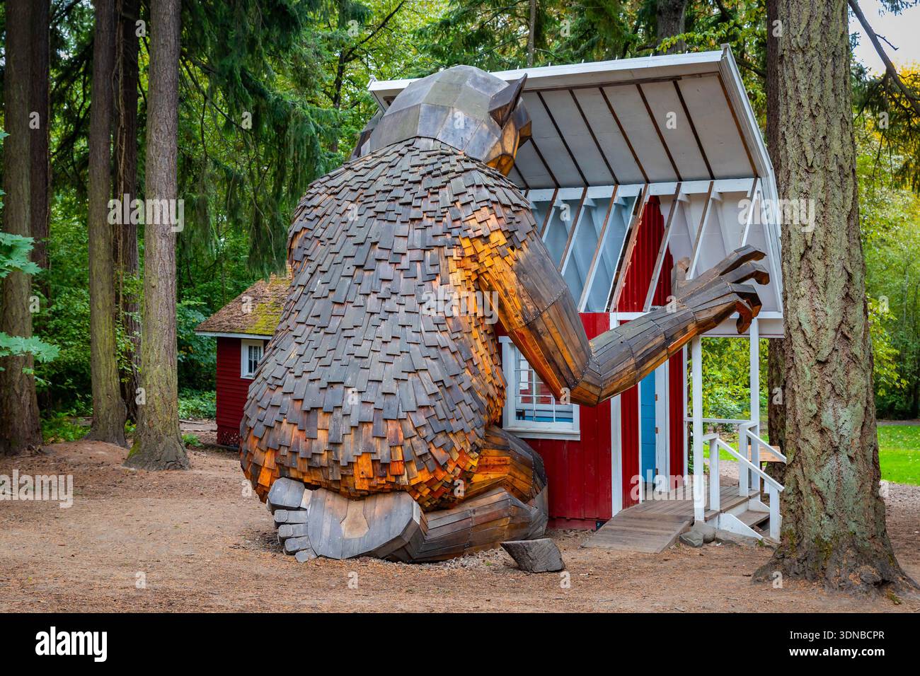 Portland, OREGON, USA - 11 ottobre 2025: Il gigante troll di Ole bolle, realizzato in legno bonificato, sbircia giocosamente in un piccolo cottage rosso sul groun di Fogelbo Foto Stock