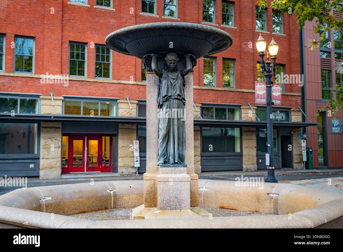 Portland, OR, USA - 9 ottobre 2025: Una pittoresca fontana cittadina si trova come punto focale in un affollato centro cittadino, circondato da un architec urbano Foto Stock
