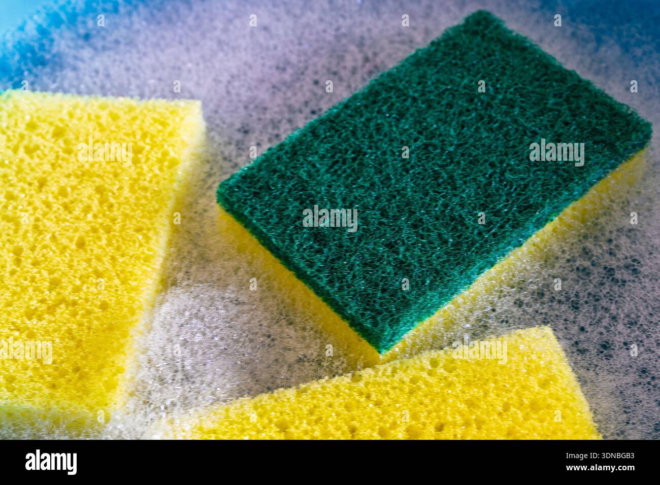 Una fotografia macro full-frame si concentra sulla consistenza di una spugna per la pulizia a due lati gialla e verde, circondata da bolle e sud di sapone bianchi, Foto Stock